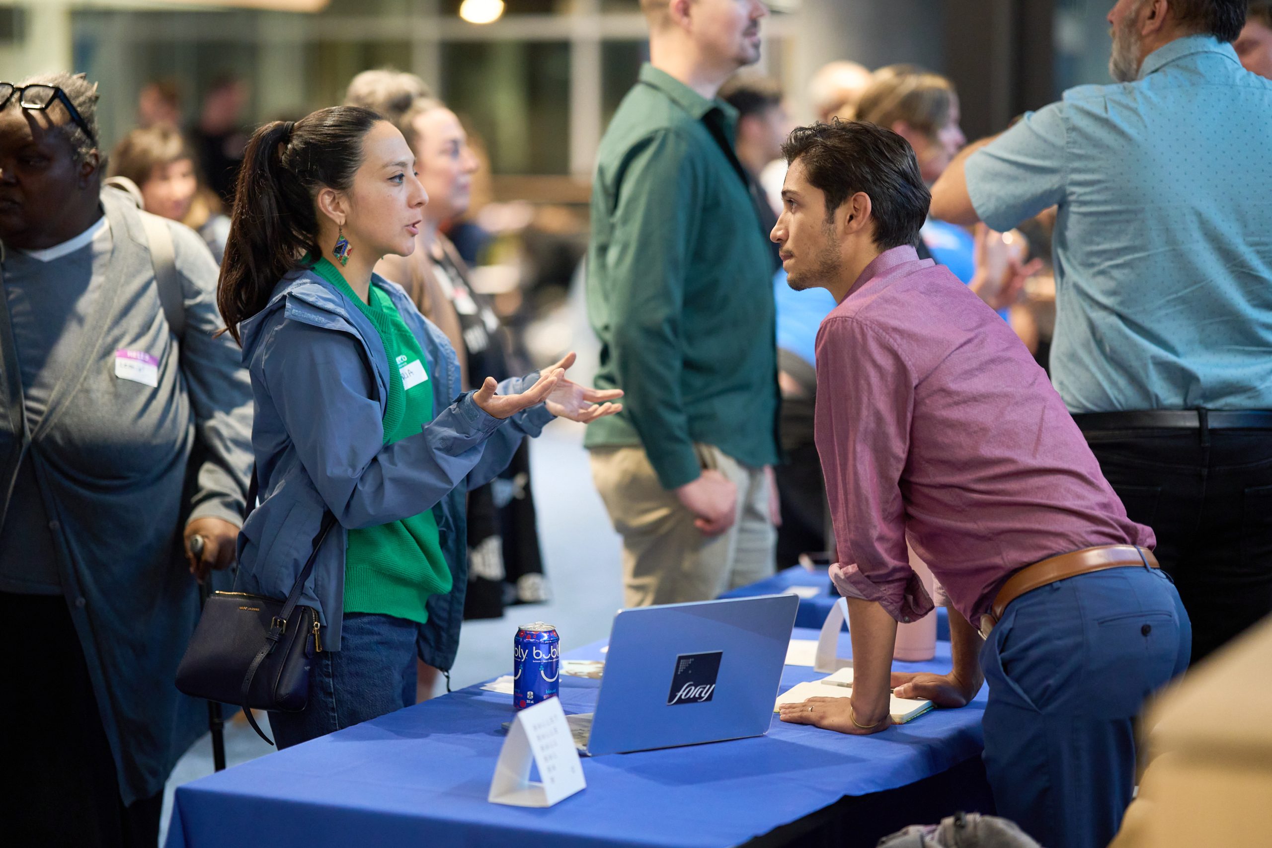 Attendees continue a conversation across a table with an open laptop after the presentations.